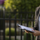 Image of real estate agent in front of a property at an open home, garden gate in the background.